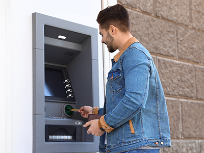 Man standing outside using ATM on the side of a building