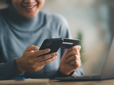 Woman smiling while using credit card and cell phone in opposite hands
