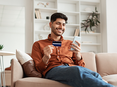 Happy man sitting on couch paying with credit card on cell phone