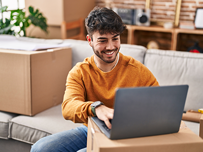 Man sitting on couch looking at laptop that is resting on moving box
