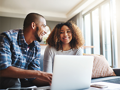 Man and women smiling at each other sitting on couch in living room across from laptop