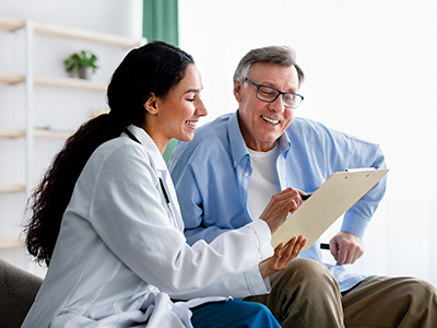 Older gentleman sitting next to young female doctor going reviewing report on clipboard