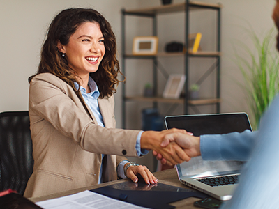 Woman reaching across table to shake hand of man sitting at desk