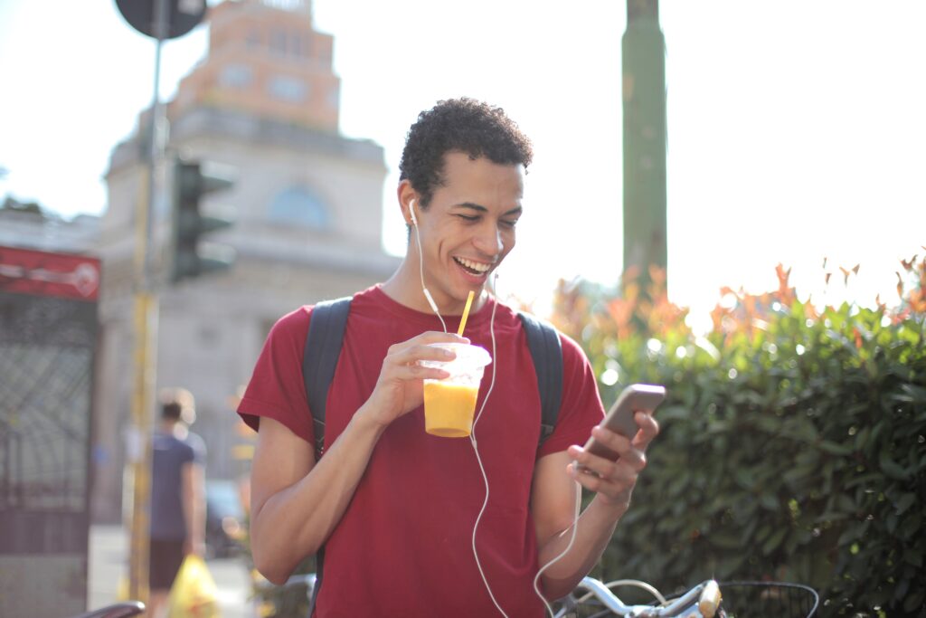 Man using his phone and drinking an orange smoothie outside.