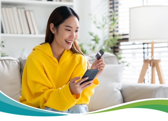 Woman wearing yellow hoodie looking at her phone and card